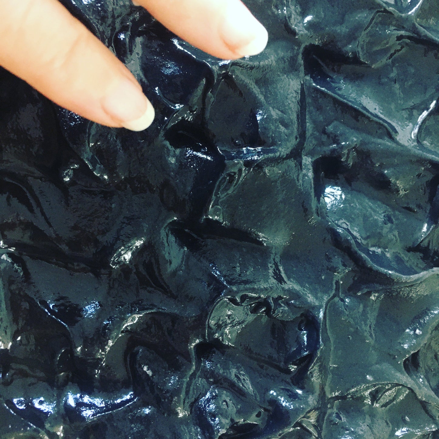 Close-up of a person's finger pointing to a textured, dark colored bar of soap.