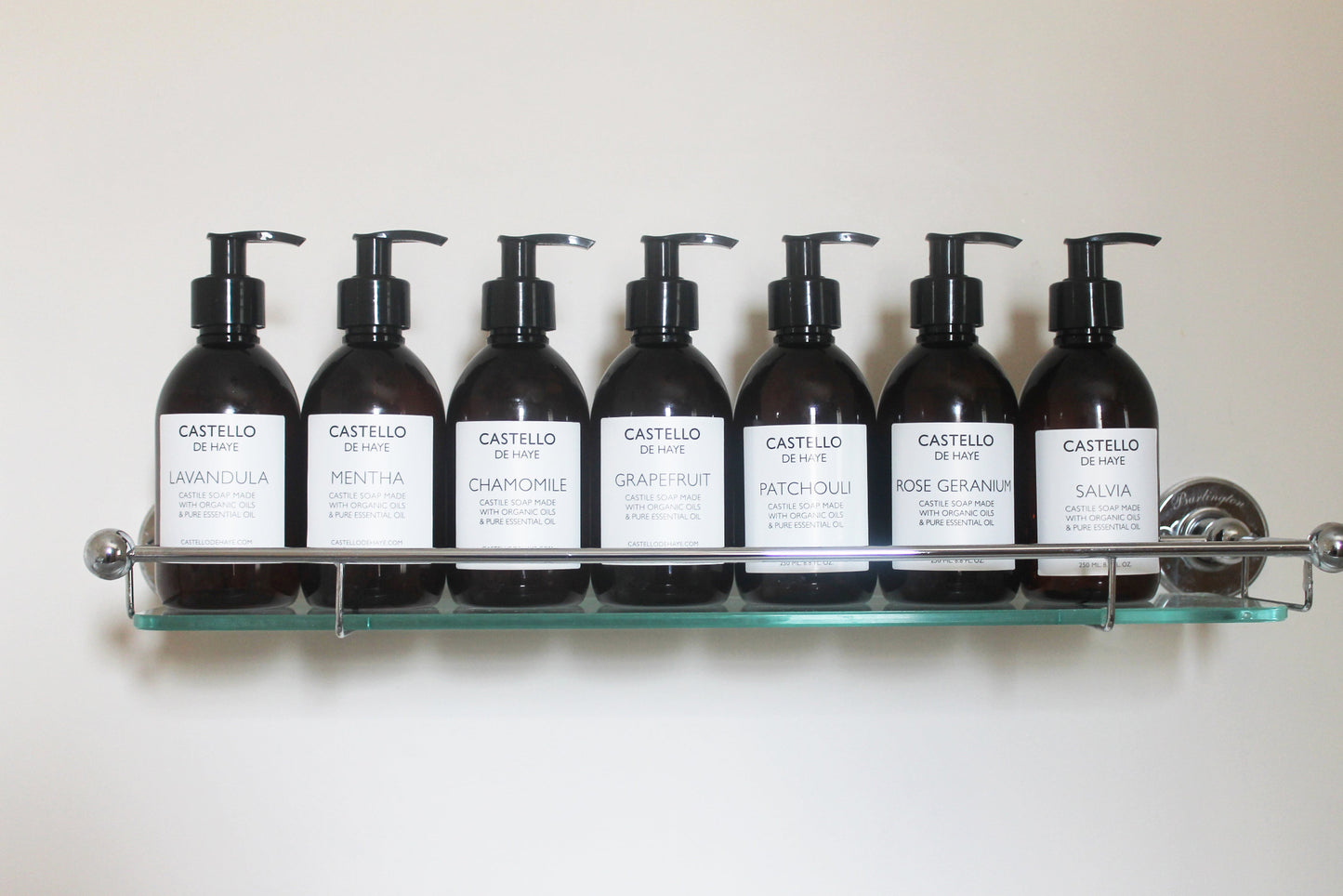 Castello de Haye row of castile soaps in pump action bottles on a bathroom glass shelf in bathroom