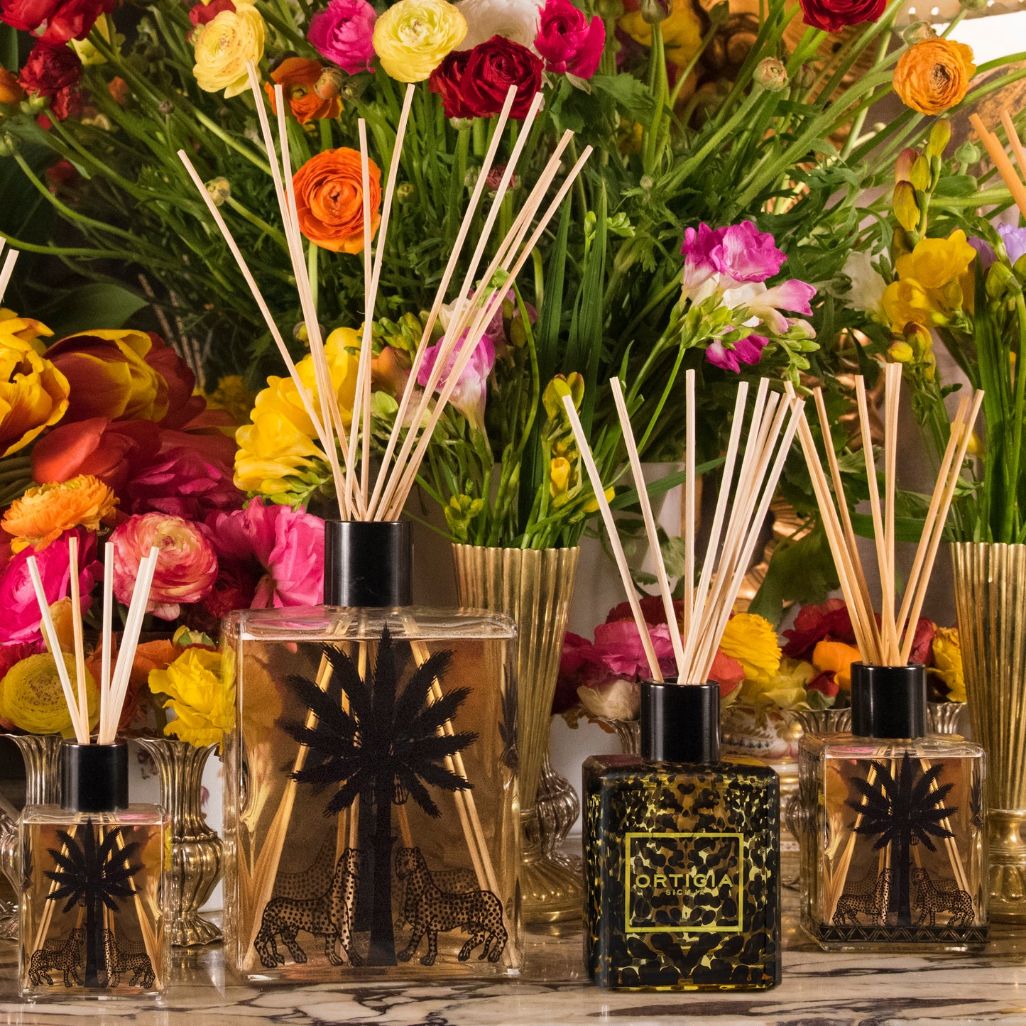 Ortigia Sicilia collection of diffusers of different sizes with beautiful flowers in the background