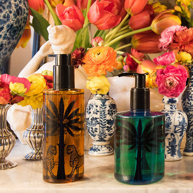 Two bottles with palm tree designs in front of colorful flowers and decorative vases.