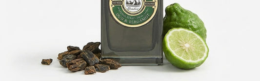 Gentlemen's Club Oud & Bergamot Eau de Toilette bottle with oud wood shards and fresh bergamot fruit on a white background