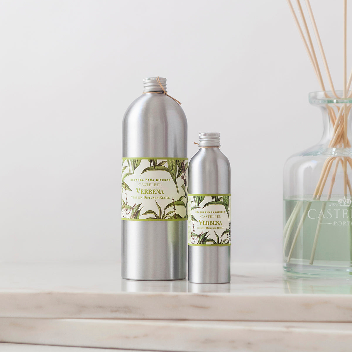 Two silver bottles with green labels on a white surface, with a glass bottle in the background.