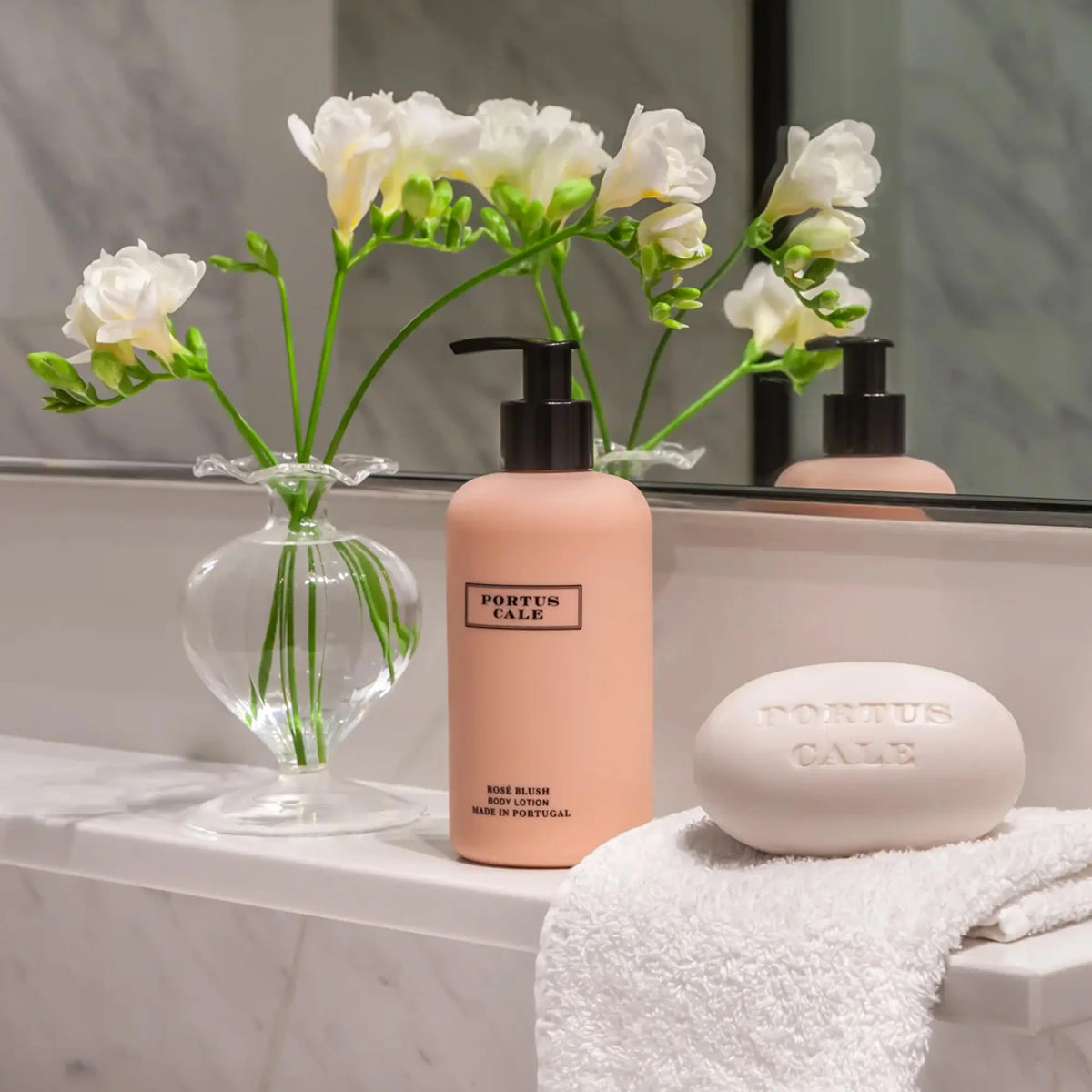 Portus Cale Rosé Blush soap bar and body lotion styled on a marble bathroom shelf with white freesias