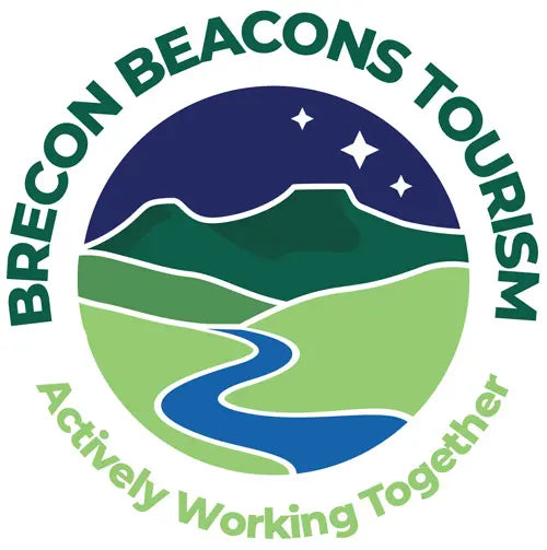 A circular logo with the words 'BRECON BEACONS TOURISM' around the top and 'Actively Working Together' around the bottom. The center shows stylized green hills, a blue winding river, and a dark blue night sky with stars.
