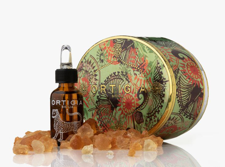 Bottle of Ortigia olive oil with a decorative container and olive stones on a white background