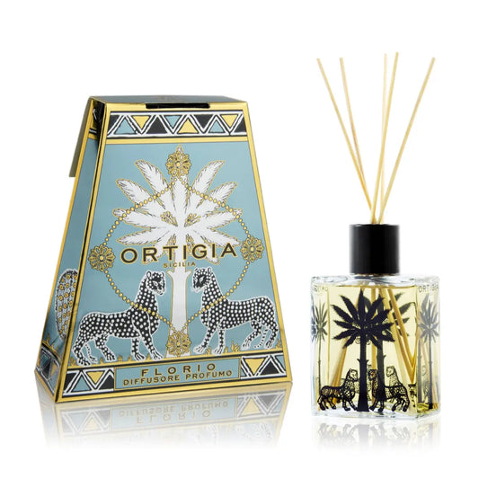 Ortigia Florio reed diffuser set featuring a decorative blue and gold box with antelope illustrations, next to a clear glass bottle with black reeds and a black cap on a white background.