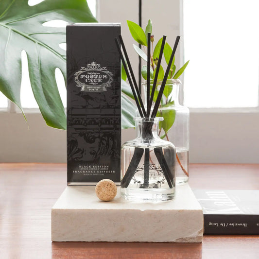 Portus Cale Black Edition reed diffuser and box on a stone display slab beside green foliage.