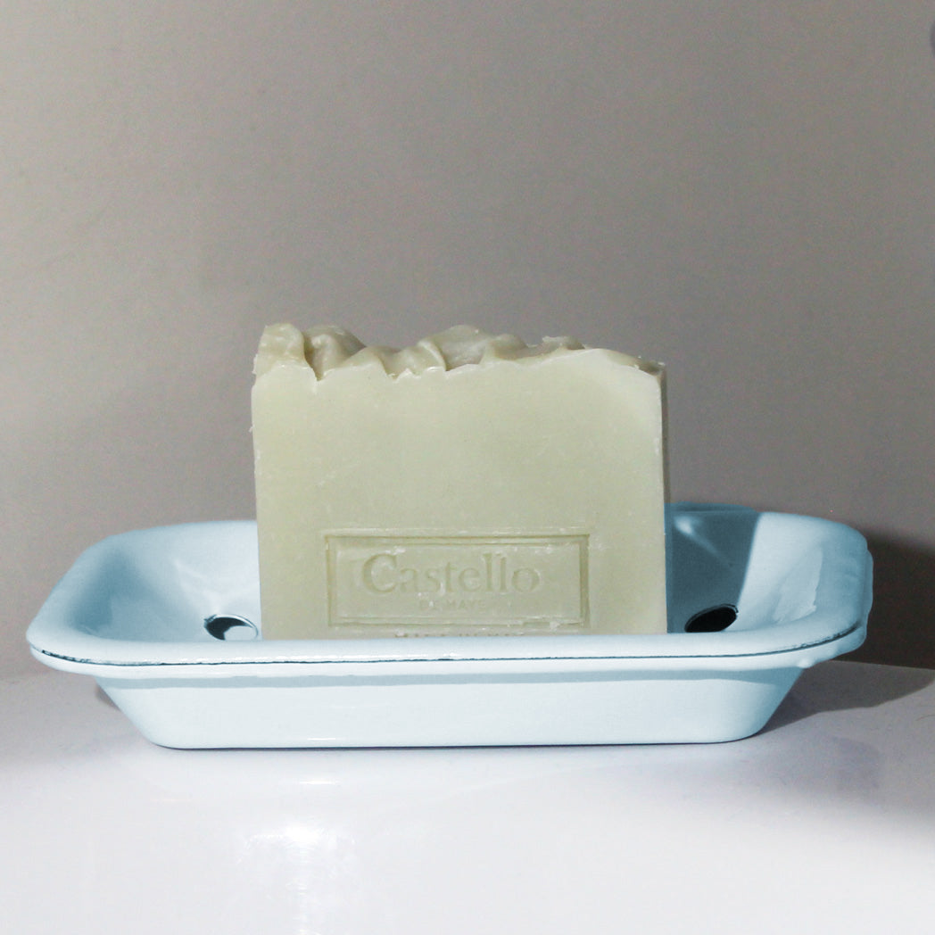 Handmade Castello de Haye soap on an enamel blue soap dish against a gray background