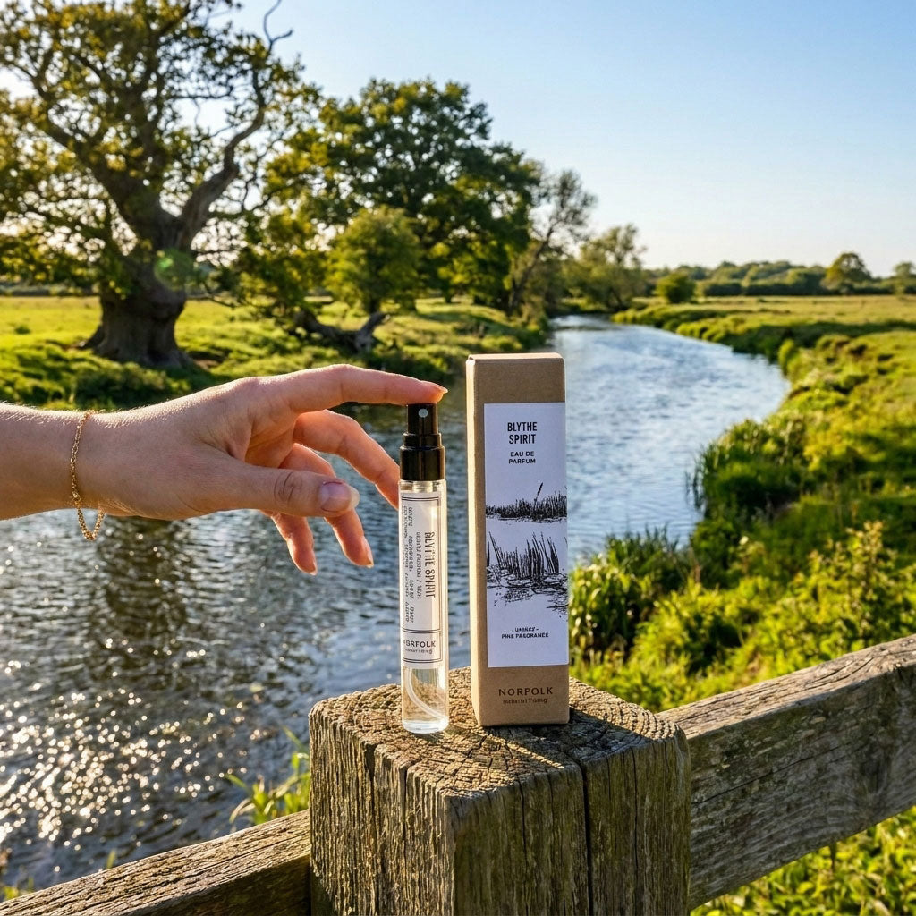 Hand touching the top of Blythe Spirit natural perfume on wooden fence with River Blyth in the background