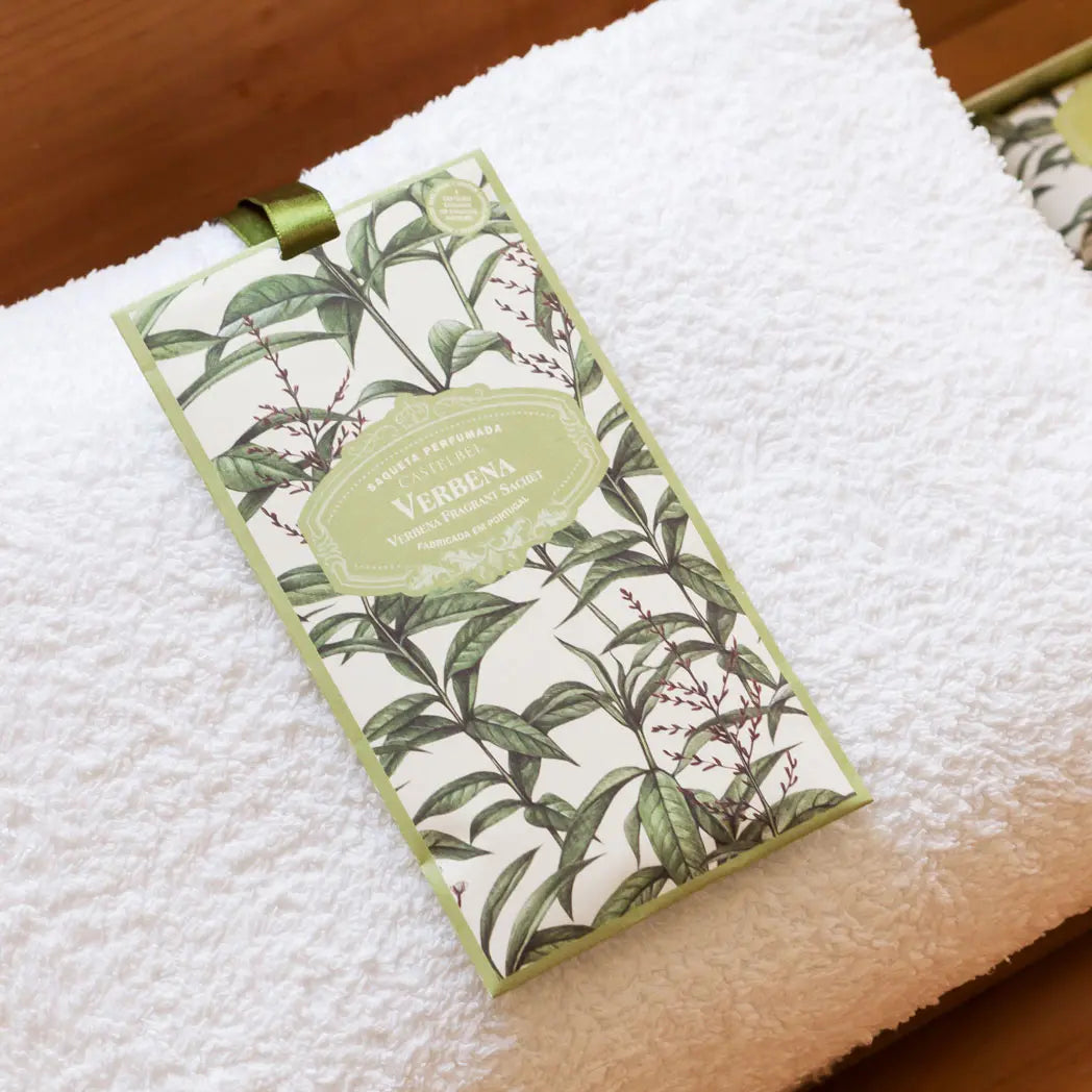 Verbena scented sachet with a botanical green and cream illustration, resting on a white textured towel over a wooden surface.