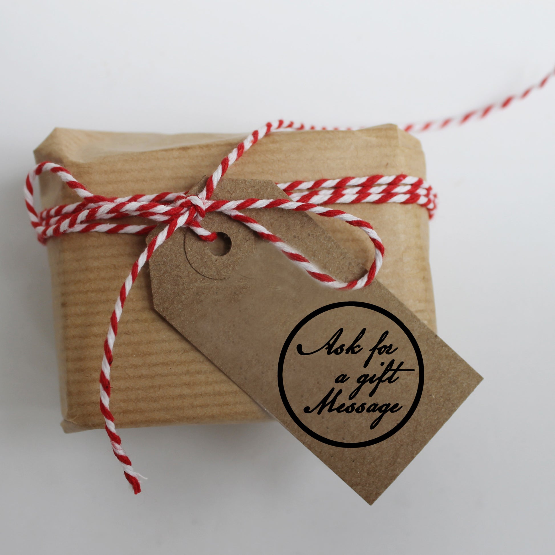 Small gift box wrapped in brown paper with red and white string and a tag on a light gray background