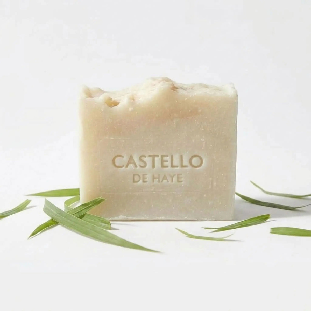 Natural cream Castello de Haye citronella soap bar with green citronella leaves on a white background