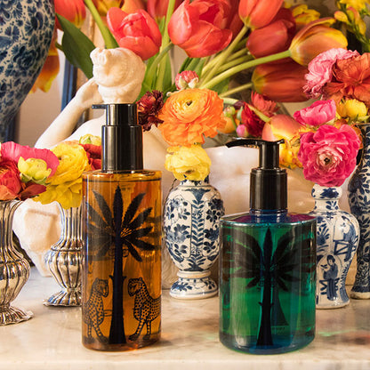 Two bottles with palm tree designs in front of colorful flowers and decorative vases.