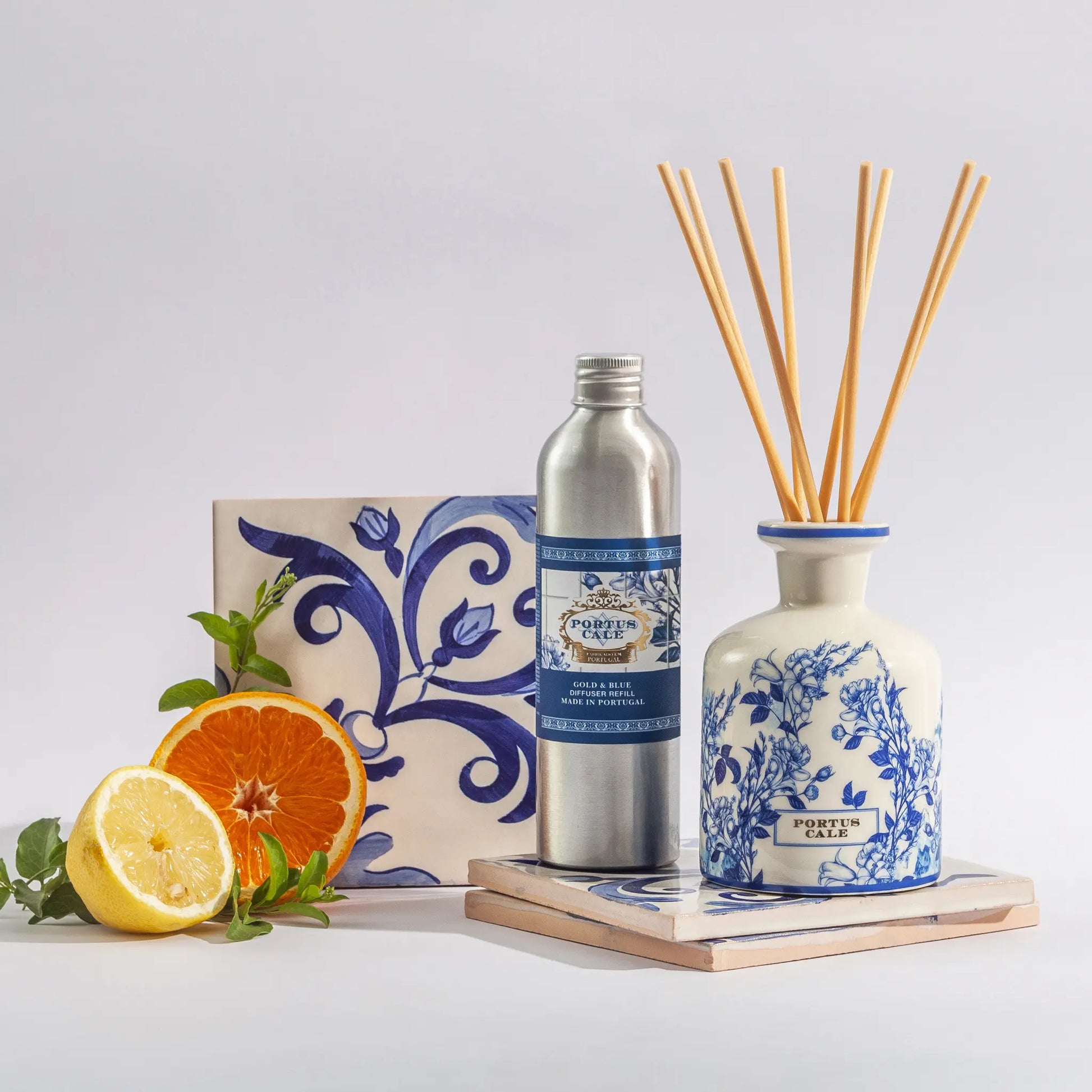 Portus Cale Gold & Blue ceramic reed diffuser 250ml and refill bottle— pink pepper and jasmine — styled with sliced orange and citrus fruit