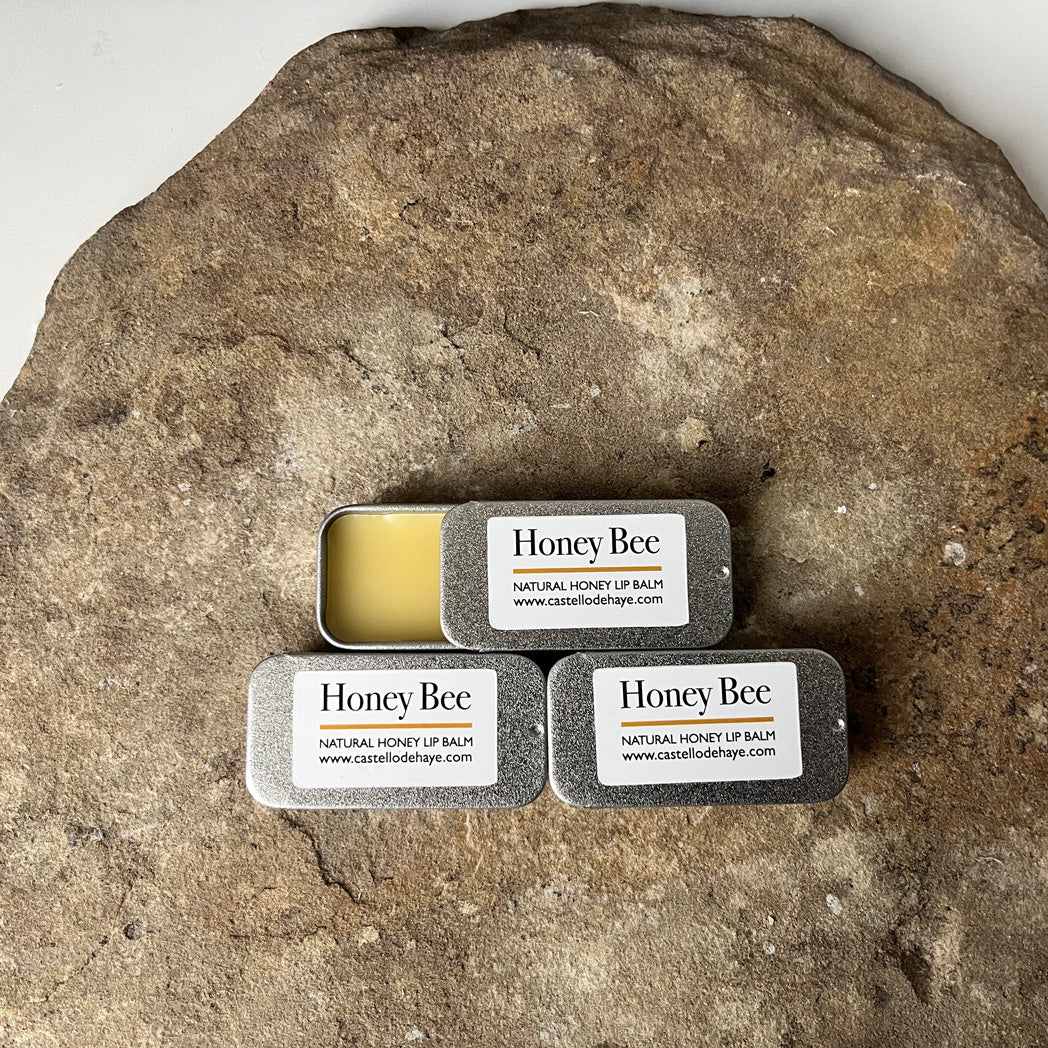 Three tins of Honey Bee lip balm on a stone surface
