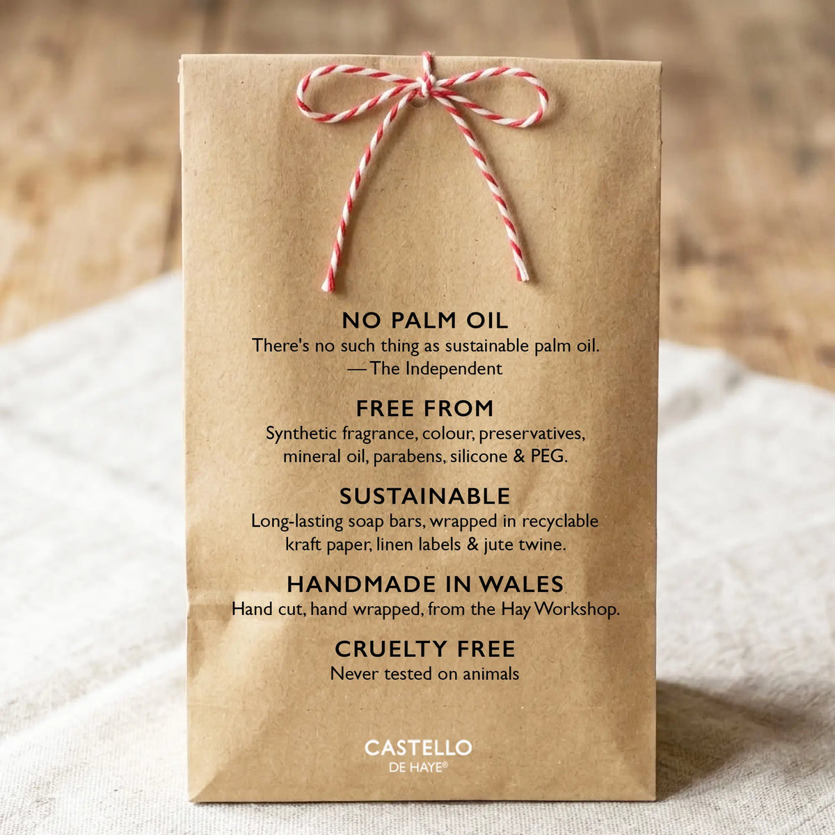 A brown kraft paper soap packaging bag tied with red and white twine, featuring black text that reads 'NO PALM OIL', 'FREE FROM', 'SUSTAINABLE', 'HANDMADE IN WALES', and 'CASTELLO De Haye logo.
