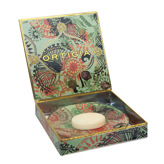 An open Ortigia Fico d'India Italian soap box with a colorful botanical pattern in sage green, coral, and black, accented with gold foil details. Inside, an oval bar of Fico d'India soap rests on a matching patterned saucer.