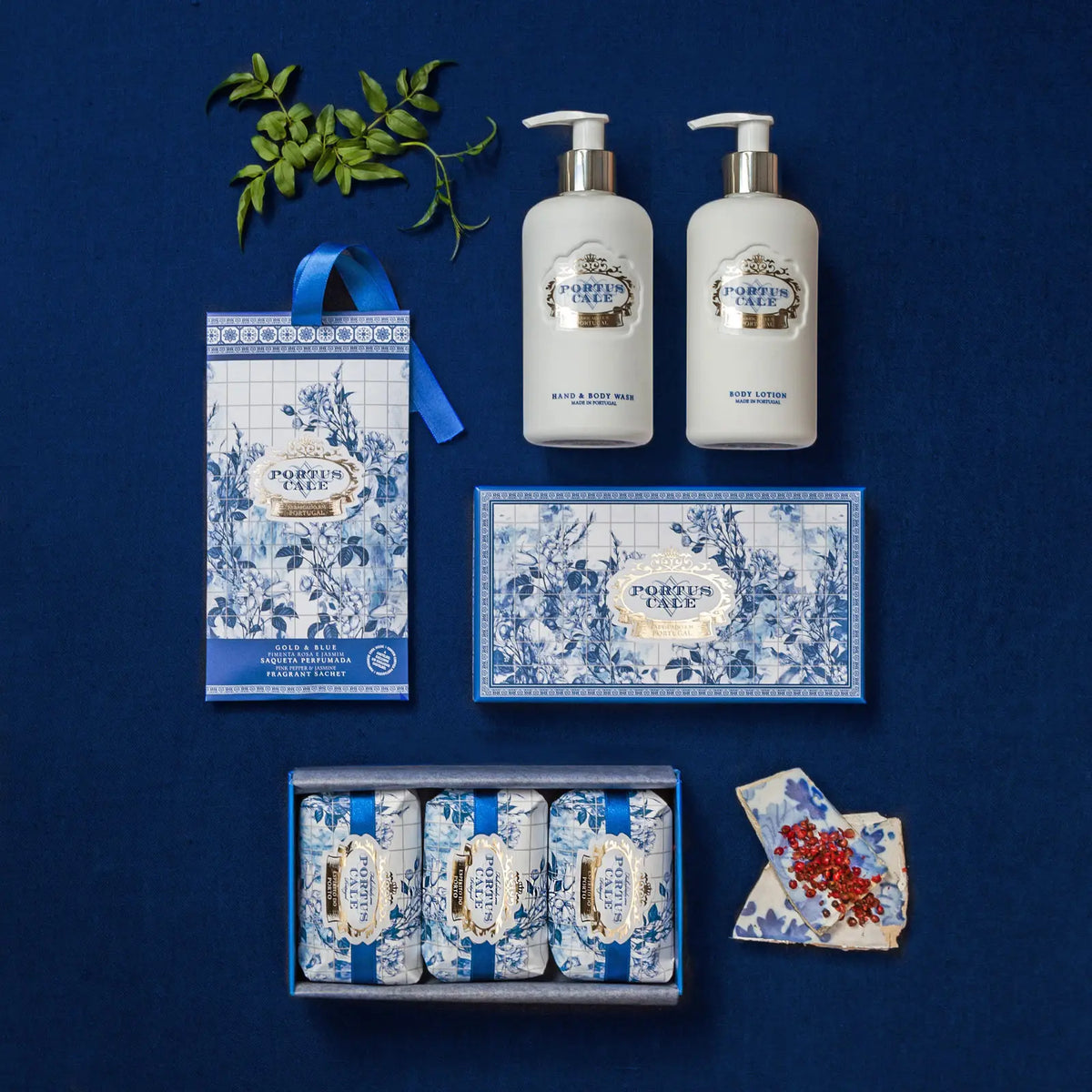 Portus Cale Gold & Blue collection flat lay with body lotion, hand & body wash, soap gift box and scented sachet on navy blue