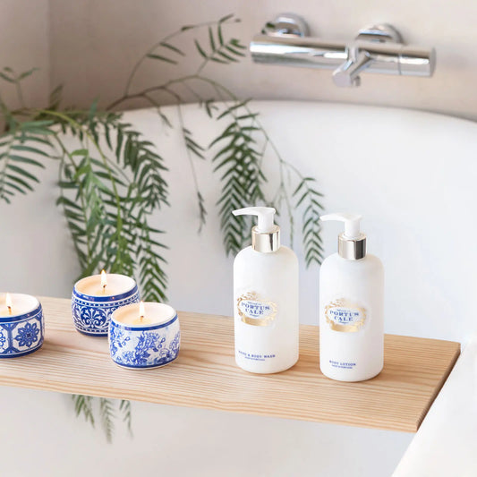 Portus Cale Gold & Blue body lotion and hand & body wash on a wooden bath tray beside blue and white ceramic candles