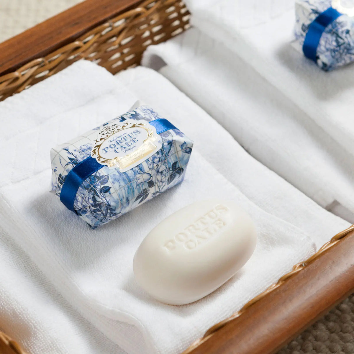 Side view of Portus Cale Gold & Blue 150g soap bar in floral wrapping, beside the unwrapped white oval soap