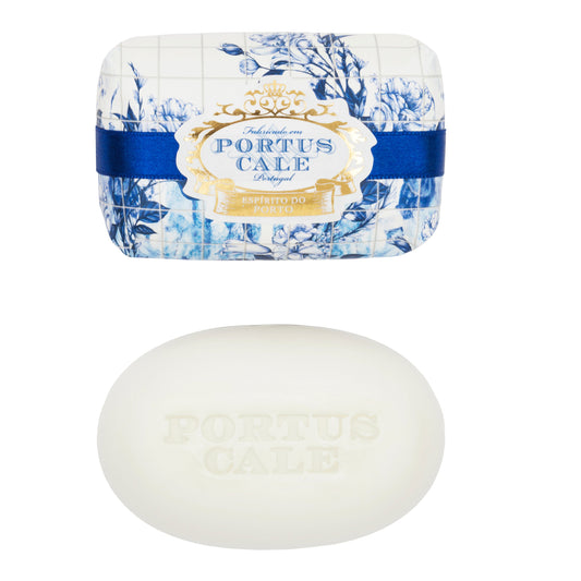 A bar of Portus Cale Gold & Blue soap with a floral design on the wrapping, alongside a plain white oval-shaped soap.