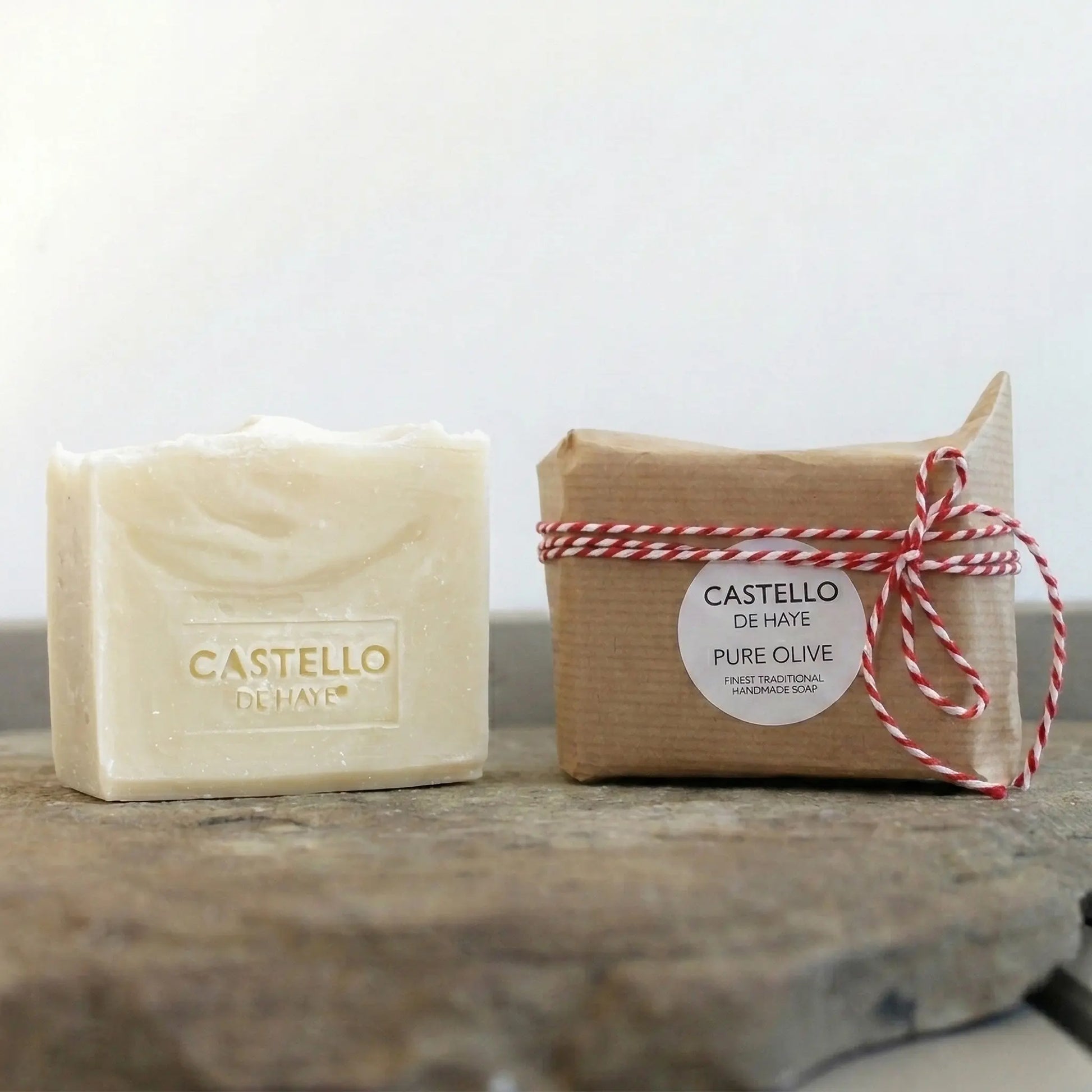 Two bars of Pure Olive soap one wrapped in kraft paper and twine and one unwrapped by Castello de Haye
