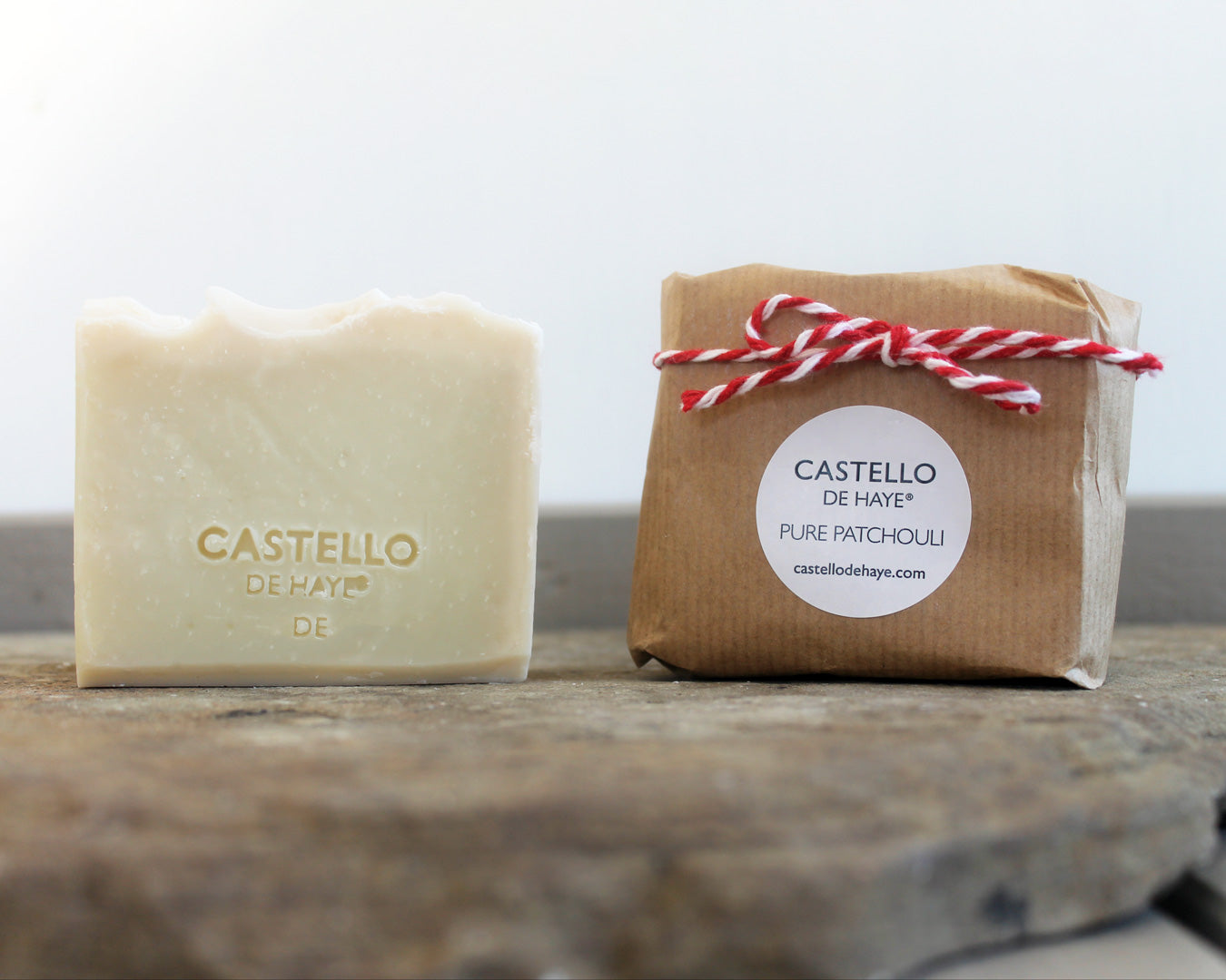 Patchouli soap bar with Castello de Haye logo beside kraft paper packaging on dark slate