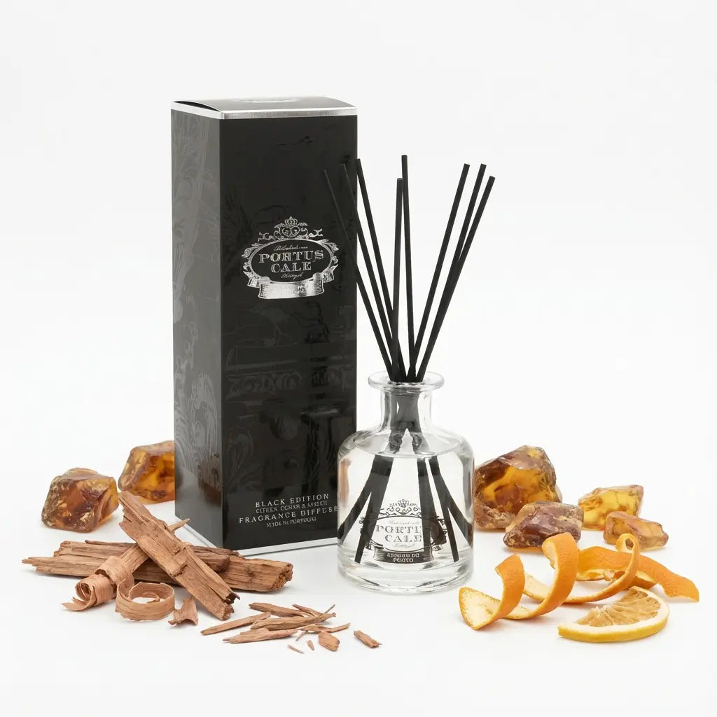 Portus Cale Black Edition reed diffuser and box surrounded by amber-coloured stones, wood shavings and orange peel.