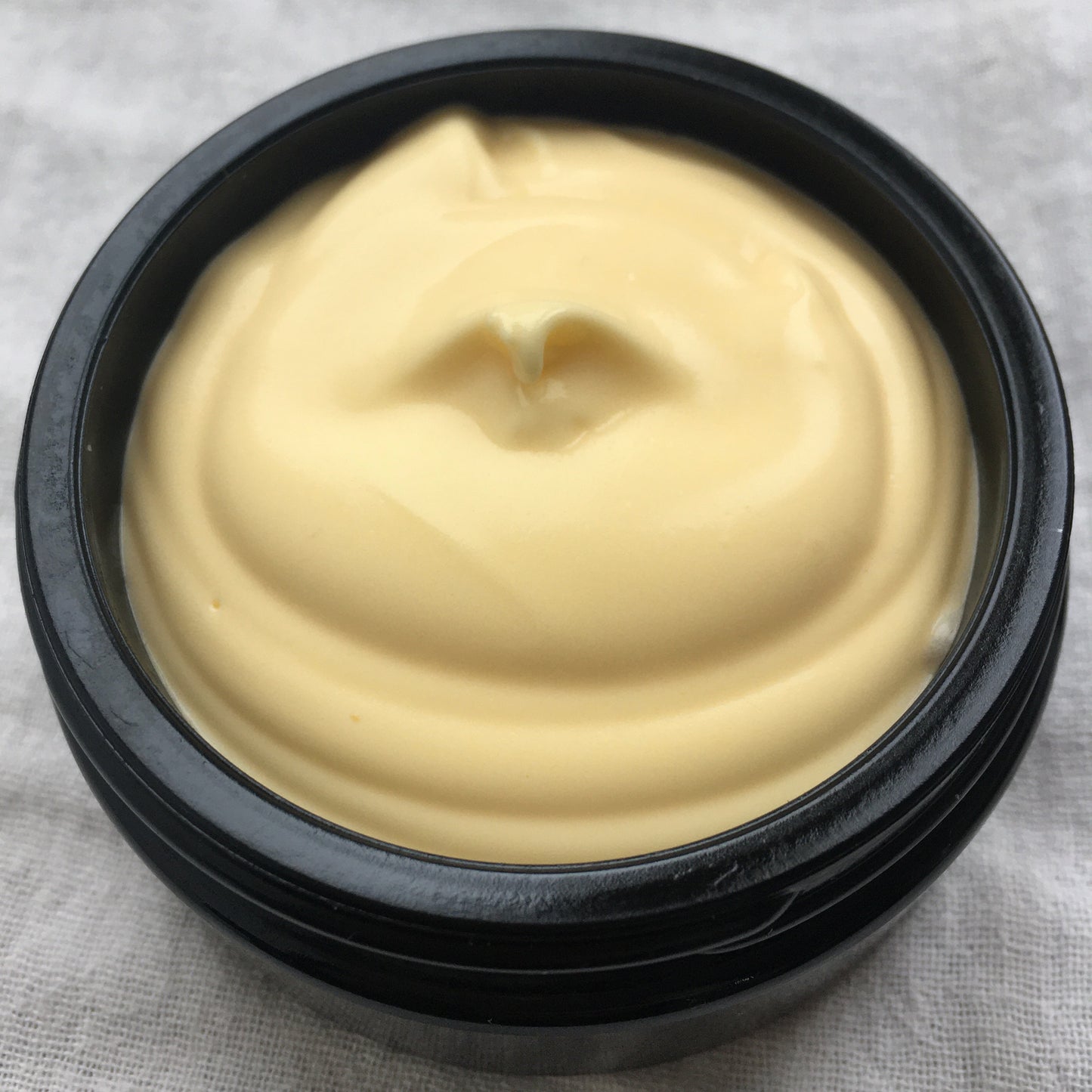 Black container with beige cream on a gray fabric background