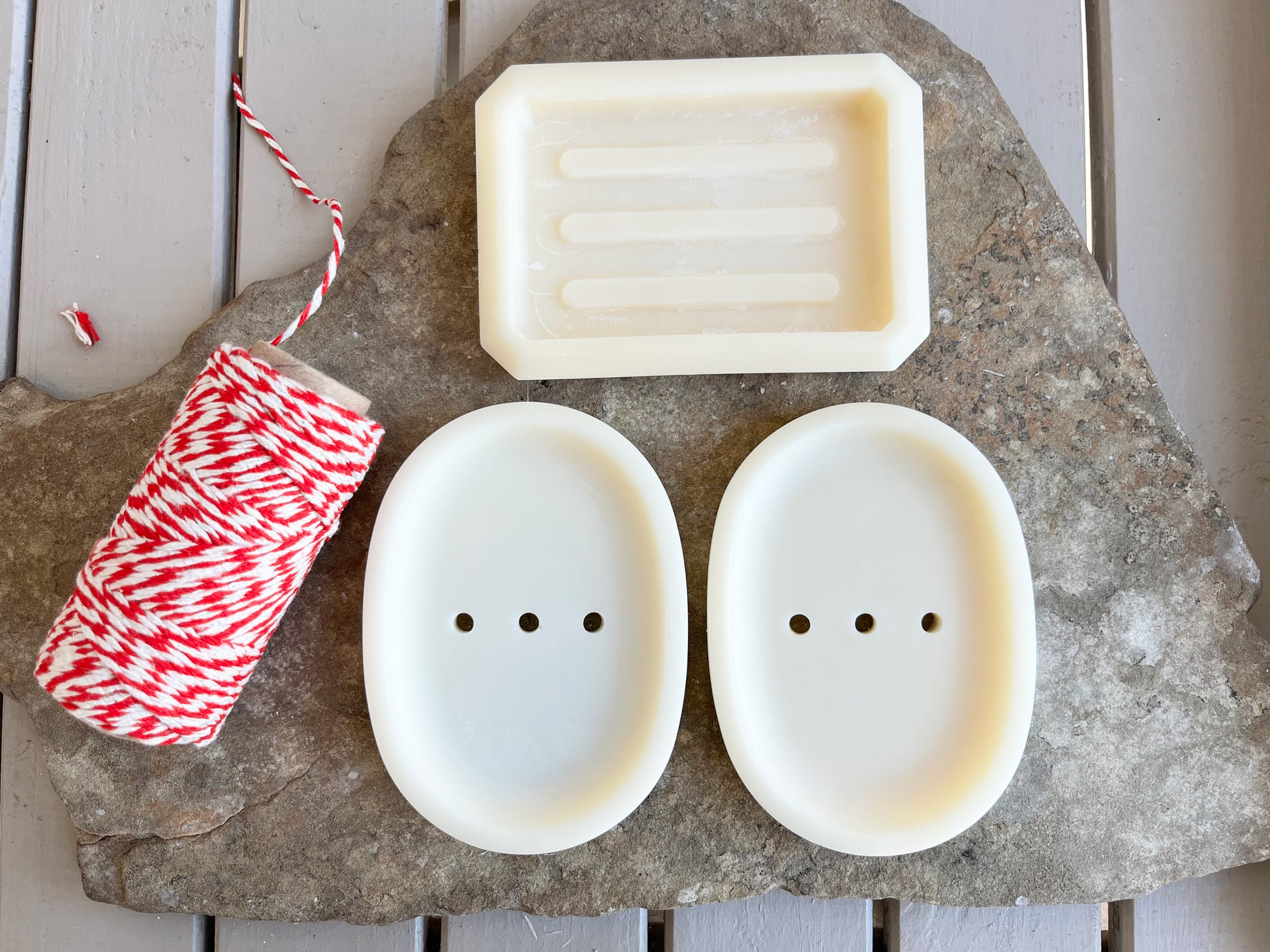 Oval and rectangular white soap dishes on a stone surface with red and white twine