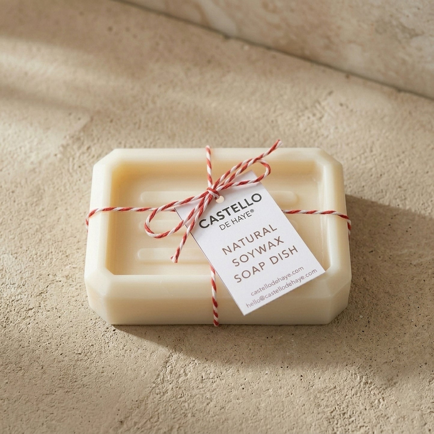 Castello de Haye oblong soy wax soap dish in white with raised ridges, tied with red and white twine on a stone background